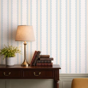 May include: A dark wood desk with a brass lamp, books, and a potted plant. The background features a wallpaper design with vertical stripes in white, light blue, and beige. The lamp has a beige lampshade.
