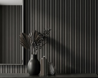 May include: A matte black vase containing dried palm leaves and dark foliage, positioned next to a stack of three books and a gray stone. The arrangement is set against a wall featuring vertical black and dark gray stripes and a rectangular mirror.