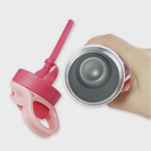 May include: A white insulated tumbler with a pink lid and straw. The lid has a light pink handle. The interior of the tumbler is silver. The straw and lid are detached from the tumbler.