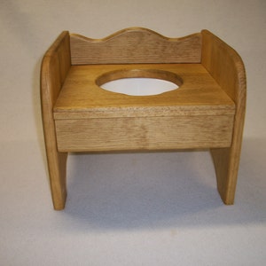 May include: A wooden potty chair with a white plastic seat and a decorative back.