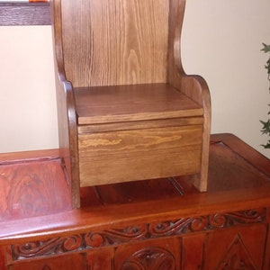 May include: A wooden child's chair with a storage compartment underneath. The chair is brown and has a simple design. It is sitting on top of a carved wooden chest.