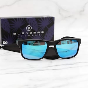 May include: Black sunglasses with blue mirrored lenses on a black case. A box with the brand name "Blenders Eyewear" is in the background. The sunglasses have a square frame.