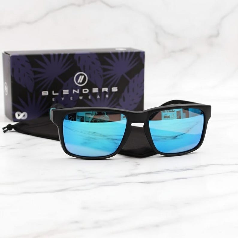 May include: Black sunglasses with blue mirrored lenses on a black case. A box with the brand name "Blenders Eyewear" is in the background. The sunglasses have a square frame.