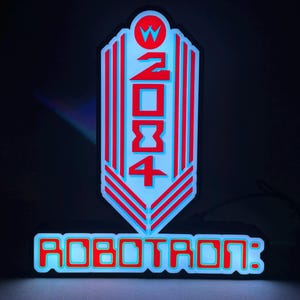 May include: A neon sign with the text "2084" and "ROBOTRON:" in red and blue. The sign has a retro, futuristic design with a stylized arrow shape and a circular element at the top. The background is dark.
