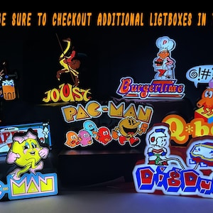 May include: A collection of illuminated arcade-themed lightboxes featuring classic characters and logos including Pac-Man, Ms. Pac-Man, Joust, BurgerTime, Q*bert, Dig Dug, and Tapper. The text at the top reads: PLEASE BE SURE TO CHECKOUT ADDITIONAL LIGTBOXES IN THE SHOP.