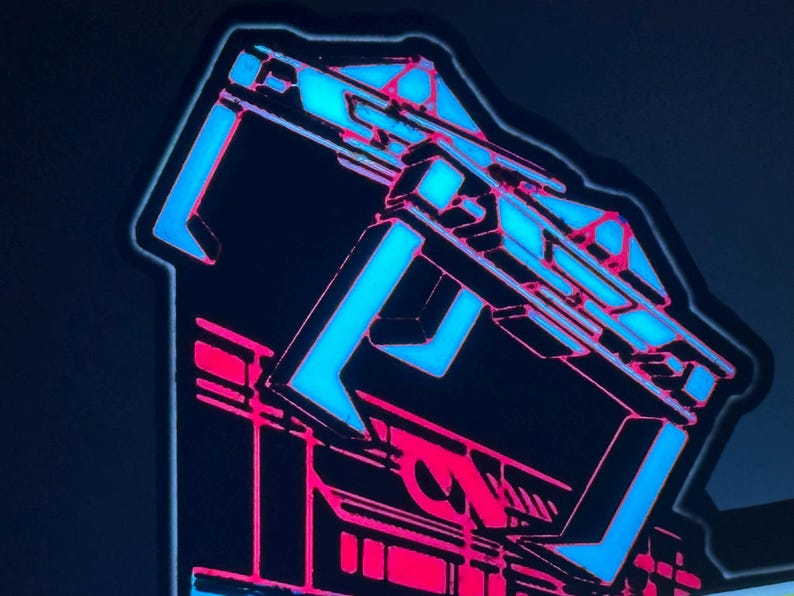 May include: A rectangular sticker featuring a stylised graphic design with a bold, bright blue geometric structure at the top and a vibrant pink architectural base. The design uses sharp lines and high-contrast colours against a dark background.
