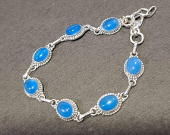 May include: A silver bracelet with oval, bright blue gemstones. The gemstones are set in decorative bezels and linked with small silver connectors. The bracelet has a lobster claw clasp for secure fastening.