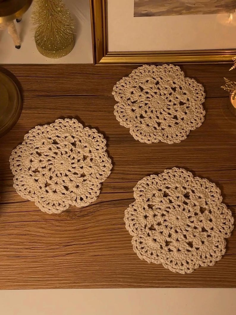 May include: Three cream-colored, handmade crochet doilies arranged on a wooden surface. Each doily has a floral design with a scalloped edge. The doilies are a neutral color, suitable for various home decor styles.