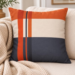 Könnte beinhalten: Ein quadratisches Dekokissen mit einem Farbblock-Design, bestehend aus einem horizontalen orangefarbenen Band oben, einem cremefarbenen Mittelteil und einem dunkelmarineblauen Unterteil, akzentuiert durch vertikale orange und dunkelblaue Streifen.