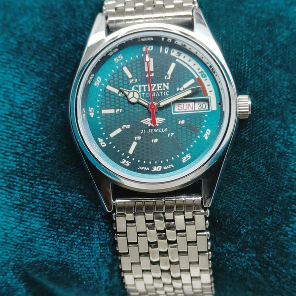 Reloj Citizen automático vintage: esfera texturizada color verde azulado, fecha y día, brazalete de acero inoxidable.