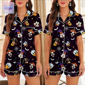 May include: Dark purple pajama set featuring a pattern of cartoon characters, including Mickey Mouse and Donald Duck, in Halloween costumes. The short-sleeved top and shorts have white trim. The pajama set is designed for comfort and style.