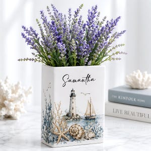 May include: A rectangular white ceramic vase filled with purple lavender sprigs. The front features a lighthouse, a sailboat, a starfish, and seashells with the name Samantha printed in black script above the nautical illustration.