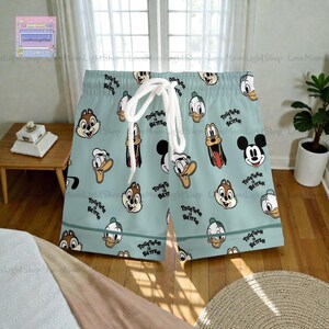 A pair of patterned shorts with cartoon duck and chipmunk faces printed on them, sitting on a wooden floor in a bedroom.