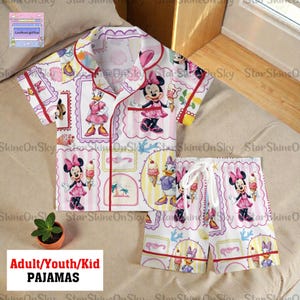 May include: White pajama set featuring Minnie Mouse and Daisy Duck illustrations. The short-sleeved top and shorts have a repeating pattern of the characters with ice cream cones and framed designs. The set is trimmed in red and includes the text "ADULT/YOUTH/KID PAJAMAS".