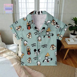 A light blue printed shirt with various cartoon character faces, including Goofy, Donald Duck, and other popular Disney characters, printed on it.