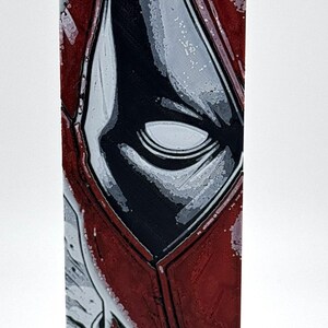 Pode incluir: Impress&atilde;o retangular em tela com um close-up da m&aacute;scara de um personagem de banda desenhada. O design apresenta um esquema de cores vermelho e preto com detalhes em branco, destacando o olho e as caracter&iacute;sticas faciais do personagem. A obra de arte tem um acabamento brilhante.
