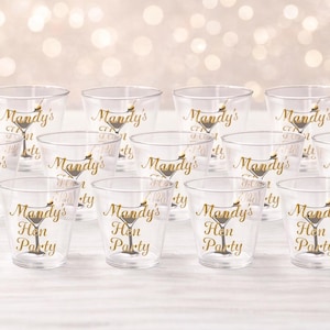 Op de afbeelding: Een set van twaalf doorzichtige plastic bekers met een goudkleurige opdruk van een martiniglas en de tekst "Mandy's Hen Party" in een sierlijk lettertype. Elke beker is identiek en in drie rijen gerangschikt voor het serveren van drankjes.