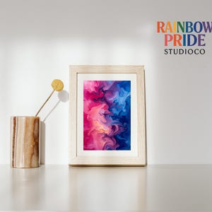 Puede incluir: Una impresión artística abstracta enmarcada con un diseño arremolinado en tonos de rosa, azul y amarillo. La obra de arte se muestra en un marco de madera de color claro. Un jarrón decorativo y una flor seca están a la izquierda del marco. El texto "RAINBOW PRIDE STUDIOCO" está en la parte superior derecha.