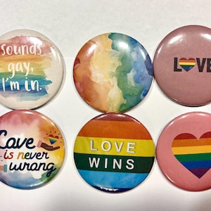 Könnte beinhalten: Eine Sammlung von sechs runden Buttons mit LGBTQ+-Pride-Designs. Die Buttons zeigen Regenbogenfarben, Herzen und Sätze wie "Sounds gay, I'm in", "Love is never wrong" und "Love Wins".
