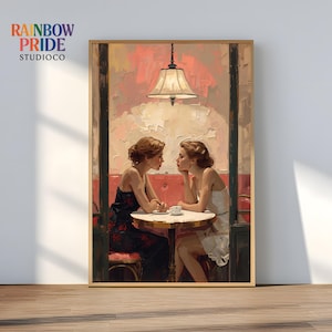 May include: A framed art print featuring two women seated at a cafe table, engaged in conversation. The artwork has a warm color palette with a focus on red and cream tones. The print includes the text "RAINBOW PRIDE STUDIOCO".