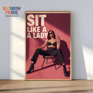 Può includere: Poster incorniciato con la scritta bianca "SIT LIKE A LADY". L'immagine mostra una persona con occhiali da sole, reggiseno nero e pantaloni neri, seduta su una sedia e con in mano un bicchiere di champagne. Lo sfondo è rosso.