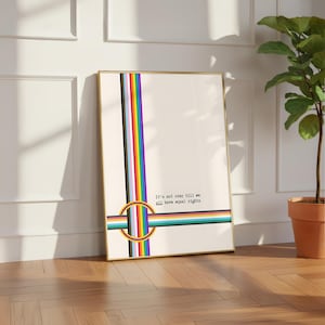 Könnte beinhalten: Ein gerahmter Druck mit goldenem Rand, der ein vertikales Regenbogenstreifen-Design zeigt. Der Druck enthält den Text "It's not over till we all have equal rights" und ein kreisförmiges Regenbogensymbol. Das Kunstwerk wird auf einem Holzboden ausgestellt.