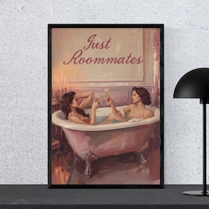 May include: A framed art print depicting two women in a bathtub, raising champagne glasses. The artwork has a vintage aesthetic, with the text "Just Roommates" above. A black lamp stands to the right.