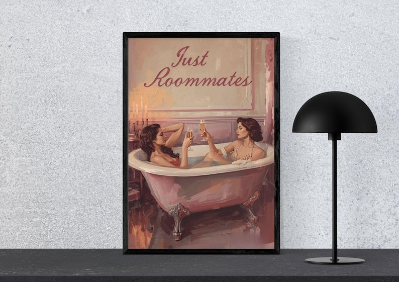 May include: A framed art print depicting two women in a bathtub, raising champagne glasses. The artwork has a vintage aesthetic, with the text "Just Roommates" above. A black lamp stands to the right.