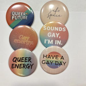 Puede incluir: Seis insignias redondas con diferentes diseños y texto. Las insignias muestran frases como "QUEER FUTURE", "Safe Space", "Gay energy", "SOUNDS GAY, I'M IN", "QUEER ENERGY" y "HAVE A GAY DAY" en varios colores.