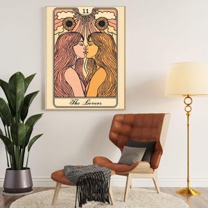 May include: A framed tarot card art print featuring two women kissing, with long flowing hair and a sunflower design. The card is labeled "The Lovers" and has the number 11 at the top. The artwork is displayed in a living room setting.