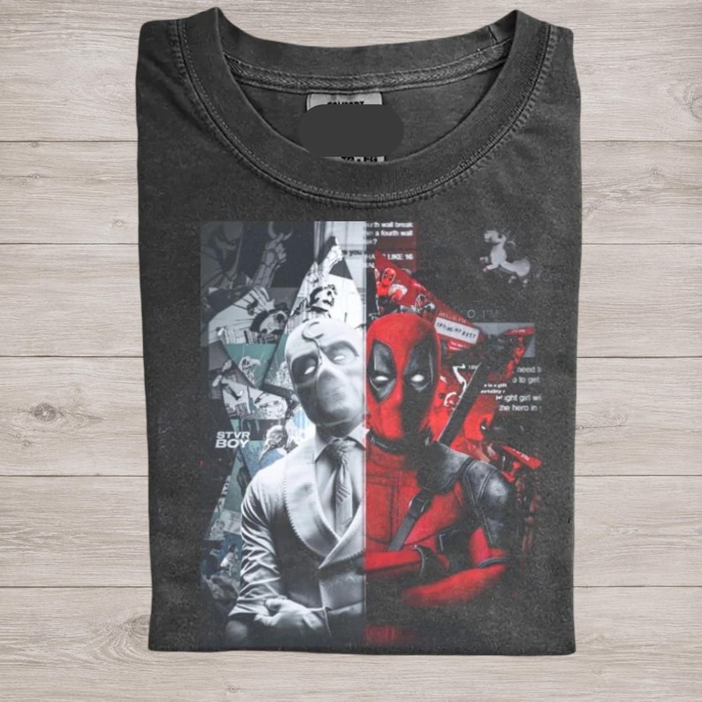 May include: Dark gray t-shirt featuring a split design with Deadpool on the right in red and a character in white on the left. The shirt has a crew neck and a graphic print.