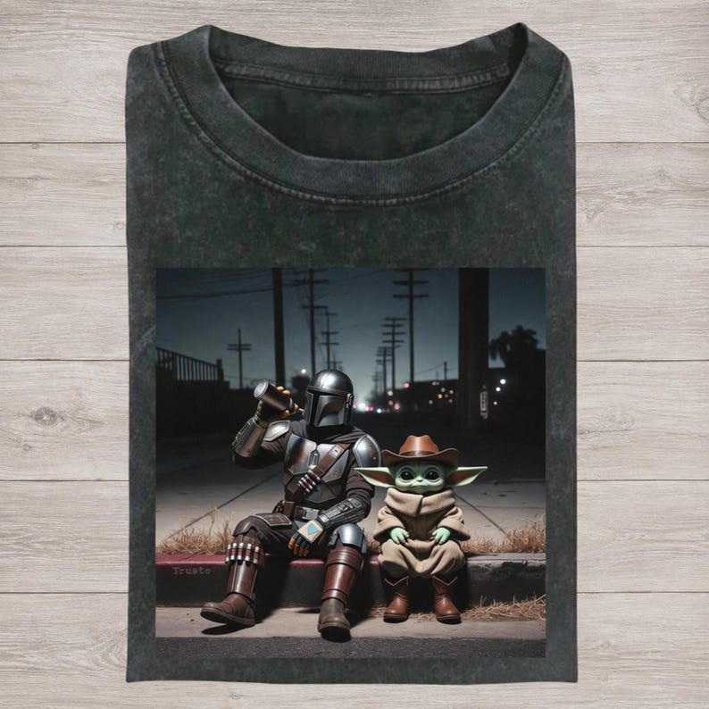 Puede incluir: Camiseta gris oscuro con un gr&aacute;fico de The Mandalorian bebiendo de una taza, sentado junto a Grogu con un sombrero de vaquero. La imagen est&aacute; ambientada en una escena callejera nocturna. La palabra "Trueto" es visible.