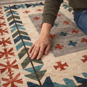 Puede incluir: Una alfombra rectangular con fondo beige y patrones geom&eacute;tricos en azul, verde y rojo. La alfombra presenta una secci&oacute;n central gris con dise&ntilde;os en forma de cruz. La alfombra est&aacute; hecha de material tejido.