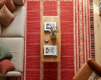May include: A large rectangular area rug featuring a vibrant red base with intricate geometric patterns in cream, black, and dark red. The design includes repeating triangular motifs, horizontal stripes, and a bold border with alternating black and red blocks.