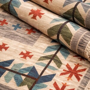 Puede incluir: Alfombra beige enrollada con un patr&oacute;n geom&eacute;trico. El dise&ntilde;o incluye cruces rojas, hojas estilizadas azules y verdes y formas rectangulares grises. La alfombra tiene un borde con flecos.