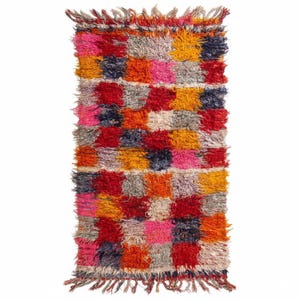 Könnte beinhalten: Ein rechteckiger, farbenfroher Teppich mit einem Patchwork-Design. Der Teppich weist eine Vielzahl von Farben auf, darunter Rot, Rosa, Orange, Gelb, Grau und Blau. Der Teppich hat eine zottelige Textur und Fransen an den Enden.