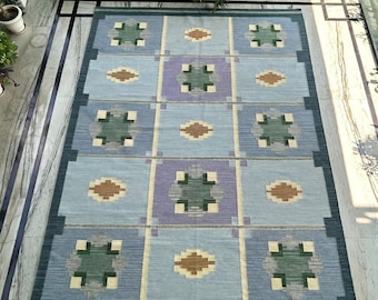 May include: A rectangular area rug with a geometric pattern. The rug features a light blue background with squares of varying colors, including green, purple, and brown. The rug has a dark blue border.