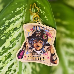 Puede incluir: Llavero de madera con una colorida ilustración de un personaje sosteniendo un cartel de "Se busca". El cartel dice "Jinx" y "Piltover Wanted" con acentos coloridos. El llavero tiene un cierre dorado y un dije de signo de la paz.