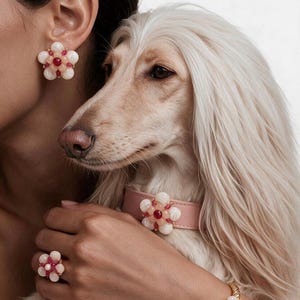 Può includere: Un set di gioielli e un collare per animali domestici con motivi floreali abbinati. Il design floreale è composto da perline bianche e rosa con una perlina rossa centrale. Il set include un orecchino, un anello, un bracciale rigido dorato intrecciato e un collare rosa.