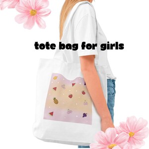 May include: White tote bag with a colorful fruit pattern, including watermelon, strawberries, and cherries. The text "tote bag for girls" is printed on the top. Pink flowers are in the background.