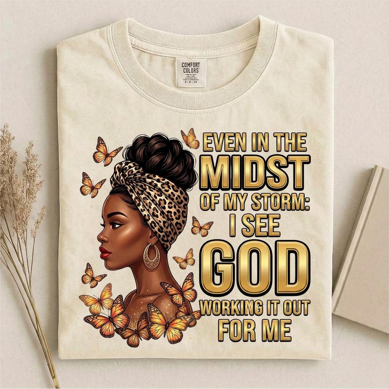 Pu&ograve; includere: T-shirt color crema con grafica di una donna con un turbante leopardato e farfalle. Il testo recita "Even in the Midst of My Storm: I See God Working It Out For Me". La maglietta ha uno scollo tondo e un'etichetta Comfort Colors.