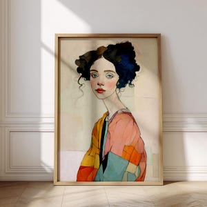 Peut inclure: Portrait à l'aquarelle encadré d'une femme aux yeux bleus et aux lèvres rouges. Elle a les cheveux bouclés foncés avec des reflets bleus et porte une veste patchwork colorée. L'œuvre est encadrée dans un cadre en bois clair.