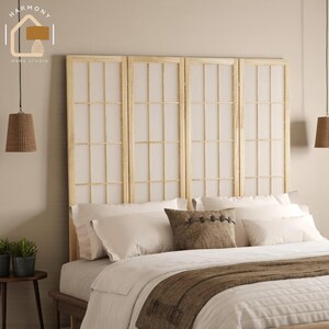 May include: A light wood headboard with four panels, each featuring a grid pattern with white paper inserts. The bed is made with white bedding, a brown throw, and decorative pillows. Two woven pendant lights hang from the ceiling.