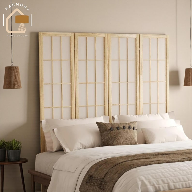 May include: A light wood headboard with four panels, each featuring a grid pattern with white paper inserts. The bed is made with white bedding, a brown throw, and decorative pillows. Two woven pendant lights hang from the ceiling.