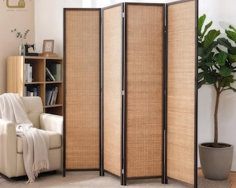 May include: A four-panel room divider with a woven, light brown texture. The frame is dark brown. The divider is standing on a light-colored rug. A potted plant is to the right of the divider. The divider is in a room with a chair and bookshelf.