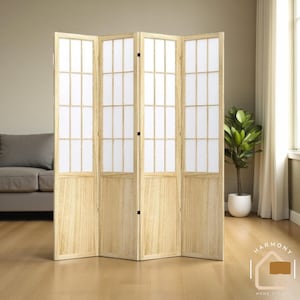 May include: A four-panel room divider with a light wood frame and white paper inserts. The divider is standing in front of a neutral-colored wall and a sofa. A potted plant is visible to the right. The divider is a home decor item.