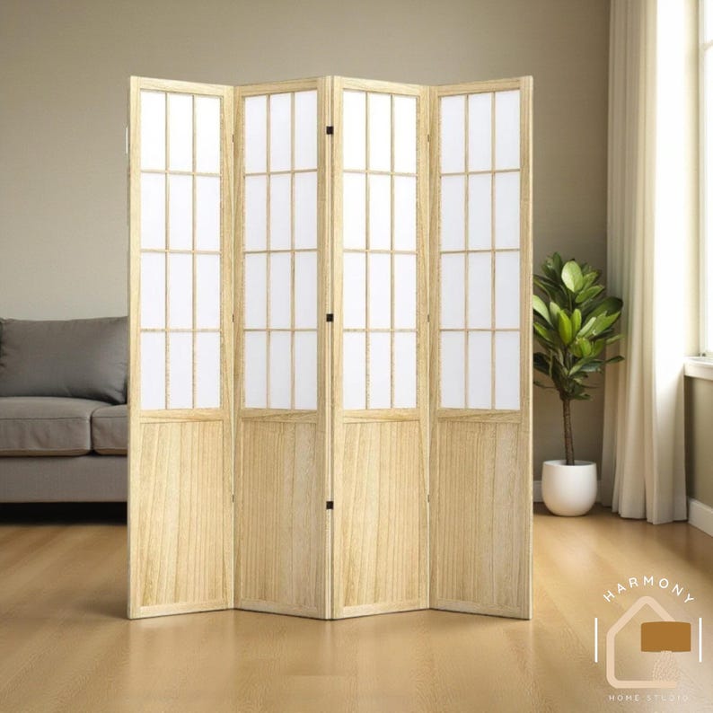 May include: A four-panel room divider with a light wood frame and white paper inserts. The divider is standing in front of a neutral-colored wall and a sofa. A potted plant is visible to the right. The divider is a home decor item.
