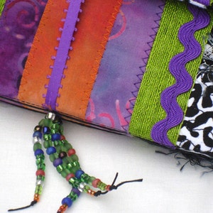 May include: A purple, orange, and green fabric patchwork with a beaded tassel. The fabric is sewn together with a zig-zag stitch.