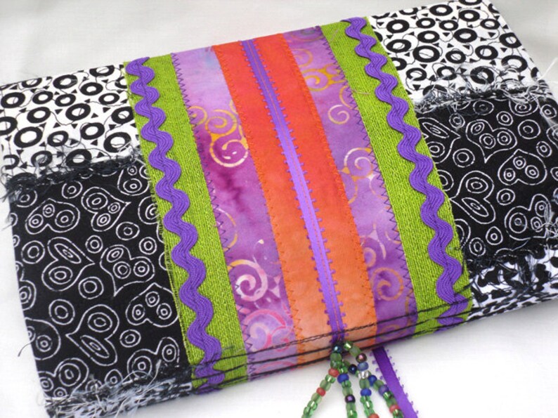 May include: A colorful patchwork fabric pouch with a purple, green, and orange ribbon trim. The pouch has a black and white patterned fabric with a fringe edge. A beaded tassel hangs from the bottom of the pouch.