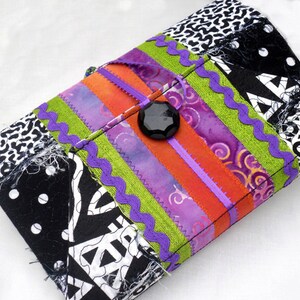 May include: A black and white patchwork fabric clutch with a purple, green, and orange striped design. A black button is in the center of the clutch.